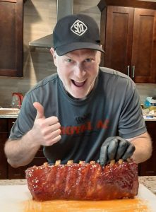 SDQ Pitmaster Paul Hirsch with a rack of beautiful pork spare ribs giving the thumbs up